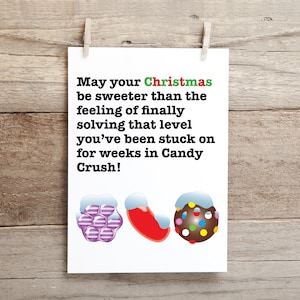 Puede incluir: Una tarjeta de Navidad con un mensaje divertido sobre Candy Crush. La tarjeta presenta un fondo blanco con texto negro y tres ilustraciones que parecen caramelos con nieve blanca en la parte superior. El texto dice: "¡Que tu Navidad sea más dulce que la sensación de resolver finalmente ese nivel en el que has estado atascado durante semanas en Candy Crush!"