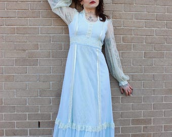 Puede incluir: Un vestido maxi azul claro con mangas largas de encaje transparente y un ribete de encaje blanco. El vestido tiene un corpiño ajustado y una falda fluida con varias capas.