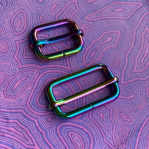 May include: Two iridescent metal slider buckles. The buckles are rectangular with a rounded edge and have a shiny, rainbow-like finish.