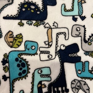 May include: White fabric with a repeating pattern of blue, green, and black dinosaurs. The dinosaurs are cartoon-like and have different shapes and sizes.