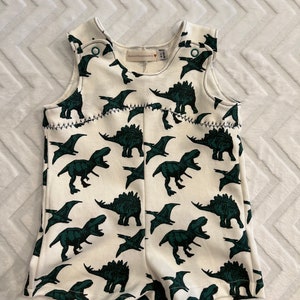 May include: White baby onesie with a green dinosaur print. The onesie has a sleeveless design and a snap closure at the crotch. The brand name "Madewell" is visible on the tag.