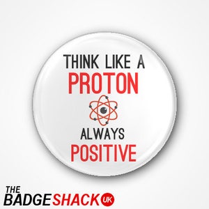 May include: A white button with the text "THINK LIKE A PROTON ALWAYS POSITIVE" in black and red. An atom graphic is in the centre. The button has a glossy finish and a shadow effect. The Badge Shack UK logo is at the bottom.