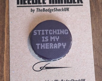 Może przedstawiać: Okrągły, fioletowy guzik z białym napisem "Stitching is my therapy". Guzik znajduje się na brązowej kartce z napisem "Needle Minder by TheBadgeShackUK" i adresem strony internetowej.