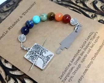 Könnte beinhalten: Ein Nadelhalter und Einfädler mit einer Vielzahl farbiger Edelsteinperlen. Der Nadelhalter hat ein silberfarbenes Lebensbaum-Design und einen Magnetverschluss. Zu den Perlen gehören Amethyst, Lapislazuli, Türkis und roter Achat.