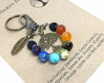 May include: A keychain with a tree of life charm and seven chakra stones, including amethyst, lapis lazuli, green sea jasper, tiger's eye, orange agate, red agate, and black onyx. The keychain also features a small feather charm.