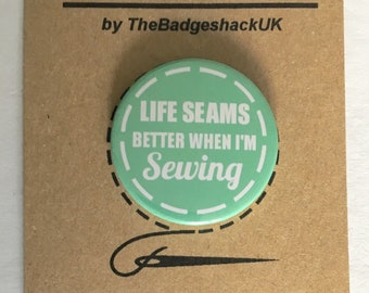Może przedstawiać: Okrągły, miętowy magnetyczny uchwyt na igłę z białym napisem "LIFE SEAMS BETTER WHEN I'M SEWING". Uchwyt na igłę znajduje się na brązowej karcie z napisem "NEEDLE MINDER" i "by TheBadgeshackUK". Na dole znajduje się grafika igły do szycia.