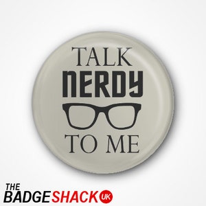 May include: A circular, pale grey badge featuring the phrase "TALK NERDY TO ME" in black, with a black glasses graphic. The badge has a shiny surface. The bottom of the badge has the text "THE BADGE SHACK UK".