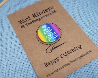 Może przedstawiać: Guzik w tęczowych kolorach z napisem "Keep Calm and Cross Stitch" i małym sercem. Guzik znajduje się na brązowej kartce z napisem "Mini Minders @TheBadgeShackUK" i "Happy Stitching www.etsy.com/shop/TheBadgeShackUk".