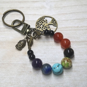 May include: A keychain with a tree of life charm, a Buddha head charm, and a beaded bracelet with seven chakra colors. The bracelet is made of black, red, orange, yellow, green, blue, and purple beads.