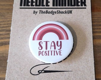 Może przedstawiać: Okrągły, biały organizer na igły z wzorem tęczy w kolorze czerwonym i różowym oraz napisem "Stay Positive".