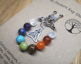 May include: A silver key chain with a silver charm of a yoga figure and seven chakra colored beads. The beads are amethyst, lapis lazuli, turquoise, green aventurine, tiger's eye, carnelian, and red jasper. The key chain also has two silver tree of life charms.