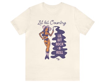 May include: A white t-shirt with a graphic of a woman in a cowboy hat painting the words "Lil Bit Rock-N-Roll" on a wall. The text "Lil bit Country" is above the graphic.