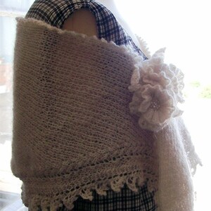 May include: A white crocheted shawl with a delicate lace trim and a large white flower accent. The shawl is draped over a black and white checked dress.