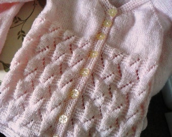 May include: A pink knitted cardigan with a button-up front and a delicate, lacy pattern. The cardigan has six white buttons.