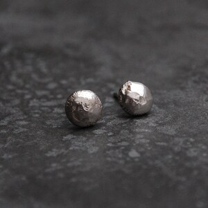 May include: A pair of silver stud earrings with a textured, hammered finish. The earrings are round and have a slightly irregular shape.