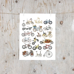 Peut inclure: Une impression d'art blanche présentant une collection d'illustrations de divers vélos à l'aquarelle, incluant un monocycle, un tandem, un vélo cargo et un grand-bi. Le texte "les Vélos" est écrit en lettres cursives dorées au centre.