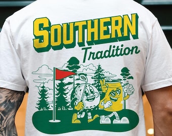 Op de afbeelding: Wit T-shirt met een groene, gele en rode afbeelding van een golfbal en een blikje bier met de tekst "Southern Tradition".