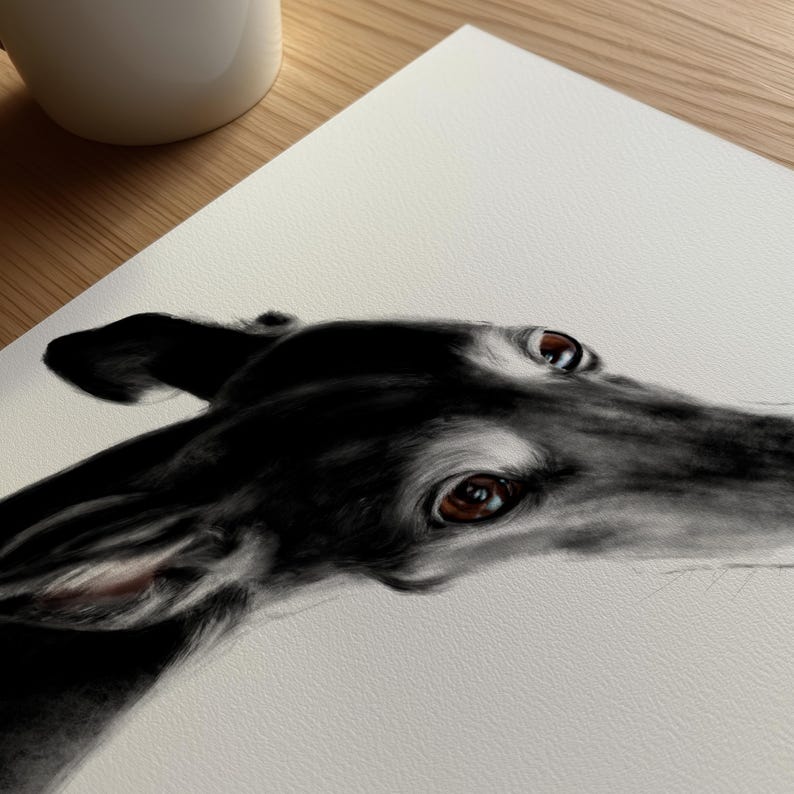 In the image: A detailed, black-and-white drawing of a greyhound's head. The dog's smooth, black coat contrasts with its brown eyes and the white paper. The artwork captures the dog's focused gaze and elegant features.