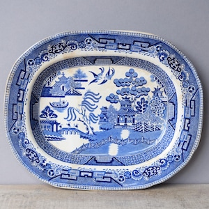 May include: Oval blue and white ceramic serving platter with a Willow pattern design. The platter features a detailed landscape scene with pagodas, bridges, and birds. The border has a decorative geometric pattern.