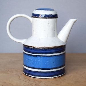 Może przedstawiać: Ceramiczny dzbanek do kawy z białym korpusem i niebiesko-białym wzorem w paski. Dzbanek ma zakrzywiony uchwyt i dzióbek. Pokrywka również ma niebiesko-biały wzór w paski.