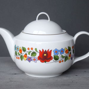 May include: White porcelain teapot with a floral design in red, orange, yellow, blue, green, and purple. The teapot has a lid and a handle.