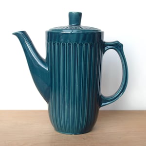 Puede incluir: Una cafetera de cerámica azul verdosa con un diseño acanalado y una tapa. La cafetera tiene un pico y una asa.