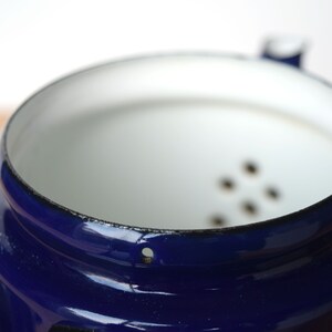 K&ouml;nnte beinhalten: Eine blaue Emaille-Kaffeekanne mit wei&szlig;em Innenraum und einem Sieb mit kleinen L&ouml;chern. Die Kanne hat einen schwarzen Rand und ein kleines Loch an der Seite.