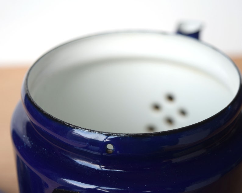 K&ouml;nnte beinhalten: Eine blaue Emaille-Kaffeekanne mit wei&szlig;em Innenraum und einem Sieb mit kleinen L&ouml;chern. Die Kanne hat einen schwarzen Rand und ein kleines Loch an der Seite.
