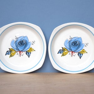 May include: Two white ceramic bowls with a blue rim and a blue rose design. The roses have yellow leaves and a red center.