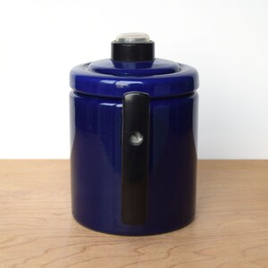 K&ouml;nnte beinhalten: Eine blaue Kaffeekanne aus Keramik mit einem schwarzen Griff und einem Deckel. Die Kanne hat ein schlichtes, klassisches Design.