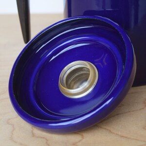 K&ouml;nnte beinhalten: Nahaufnahme eines blauen Keramikdeckels mit schwarzem Rand und einer kleinen, durchsichtigen Glas&ouml;ffnung in der Mitte. Der Deckel hat ein konzentrisches Kreisdesign.