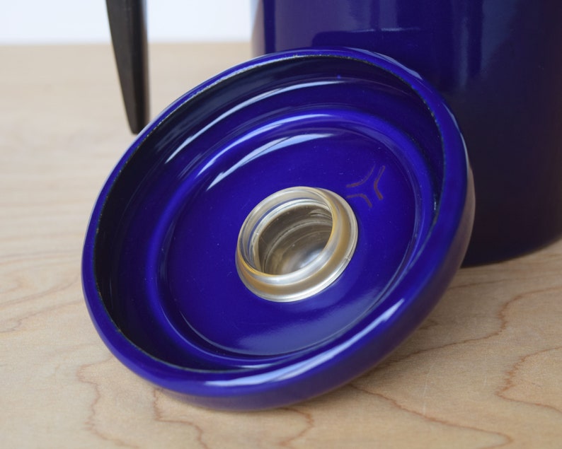 K&ouml;nnte beinhalten: Nahaufnahme eines blauen Keramikdeckels mit schwarzem Rand und einer kleinen, durchsichtigen Glas&ouml;ffnung in der Mitte. Der Deckel hat ein konzentrisches Kreisdesign.