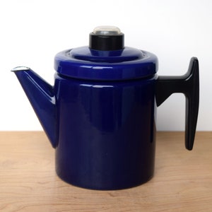 K&ouml;nnte beinhalten: Eine blaue Emaille-Kaffeekanne mit schwarzem Griff und Deckel. Die Kanne hat einen Ausguss an der Seite und einen kleinen Knopf auf dem Deckel.