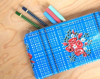 May include: A blue zippered pencil case with a white and black checkered pattern and a floral design. The case is filled with pencils and markers.