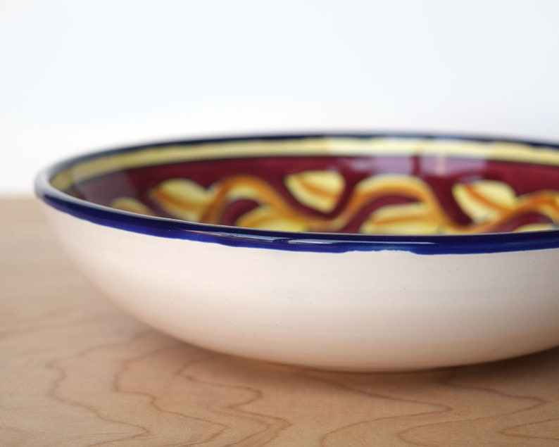 May include: A white ceramic bowl with a blue rim and a colourful design of yellow and red swirls. The bowl is on a wooden surface.
