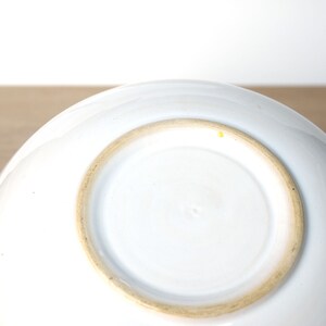 May include: White ceramic bowl with a slightly raised rim and a brown glazed base. The bowl is empty and sitting on a wooden surface.