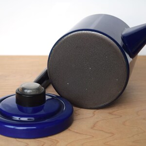 K&ouml;nnte beinhalten: Eine blaue Emailleteekanne mit einem schwarzen Deckel und einem grauen Boden. Die Teekanne hat einen Ausguss und einen Griff.