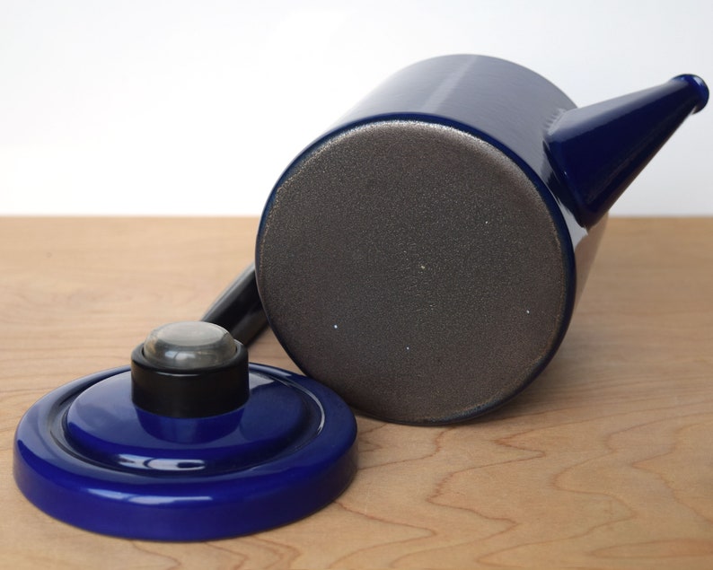 K&ouml;nnte beinhalten: Eine blaue Emailleteekanne mit einem schwarzen Deckel und einem grauen Boden. Die Teekanne hat einen Ausguss und einen Griff.