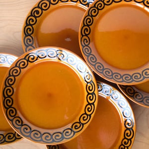 May include: Set of five brown ceramic plates with black swirl designs around the rim.
