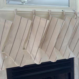 May include: Six beige and brown striped stockings hanging on a white mantel above a black fireplace.