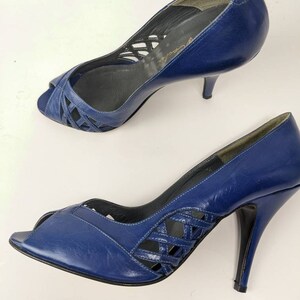 May include: A pair of blue leather peep-toe heels with a criss-cross design on the vamp. The heels are approximately 3 inches tall.