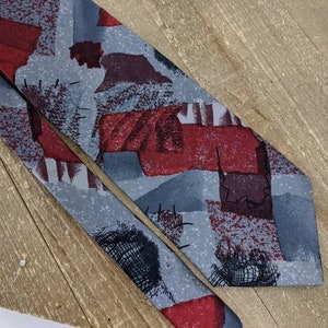 May include: A grey and red patterned tie with abstract shapes. The tie is made of a silky material and has a subtle sheen.