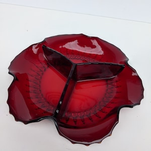 May include: A red glass serving dish with three divided sections. The dish has a scalloped edge and a textured design.