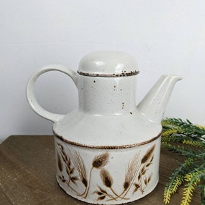 Peut inclure: Théière en céramique blanche avec un motif de blé brun. La théière a un couvercle et une poignée.