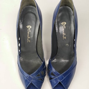 May include: A pair of blue leather peep-toe heels with a criss-cross design on the vamp. The shoes are labeled "Cackett".