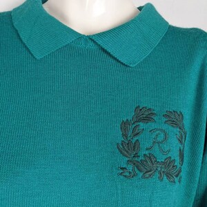 May include: Teal blue knitted sweater with a black embroidered wreath and the letter "R" in the centre.