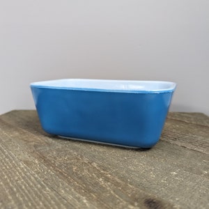 Puede incluir: Un molde para hornear rectangular azul con un borde blanco. El molde está hecho de vidrio y tiene un acabado liso y brillante.