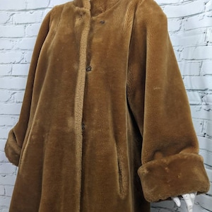 May include: A long brown faux fur coat with a high collar and button fastening. The coat has long sleeves with wide cuffs.