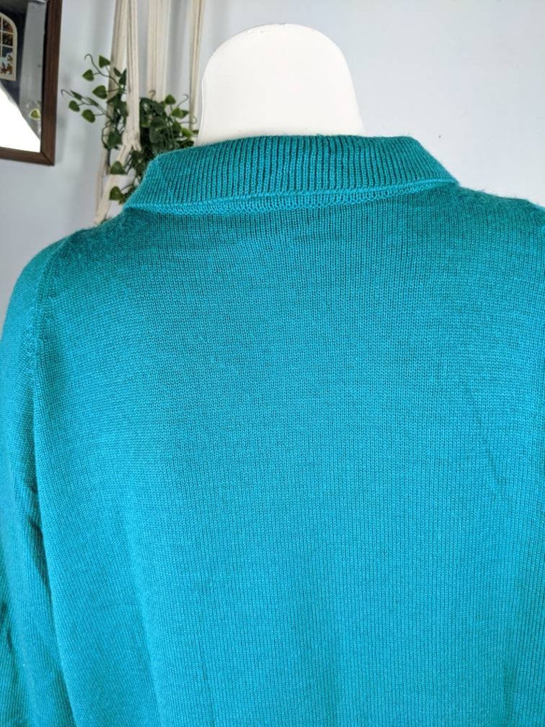 May include: A teal blue knitted sweater with a ribbed collar.