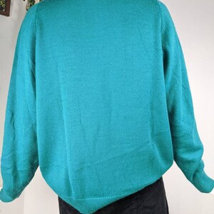 May include: A teal blue knitted sweater with long sleeves and a crew neck.